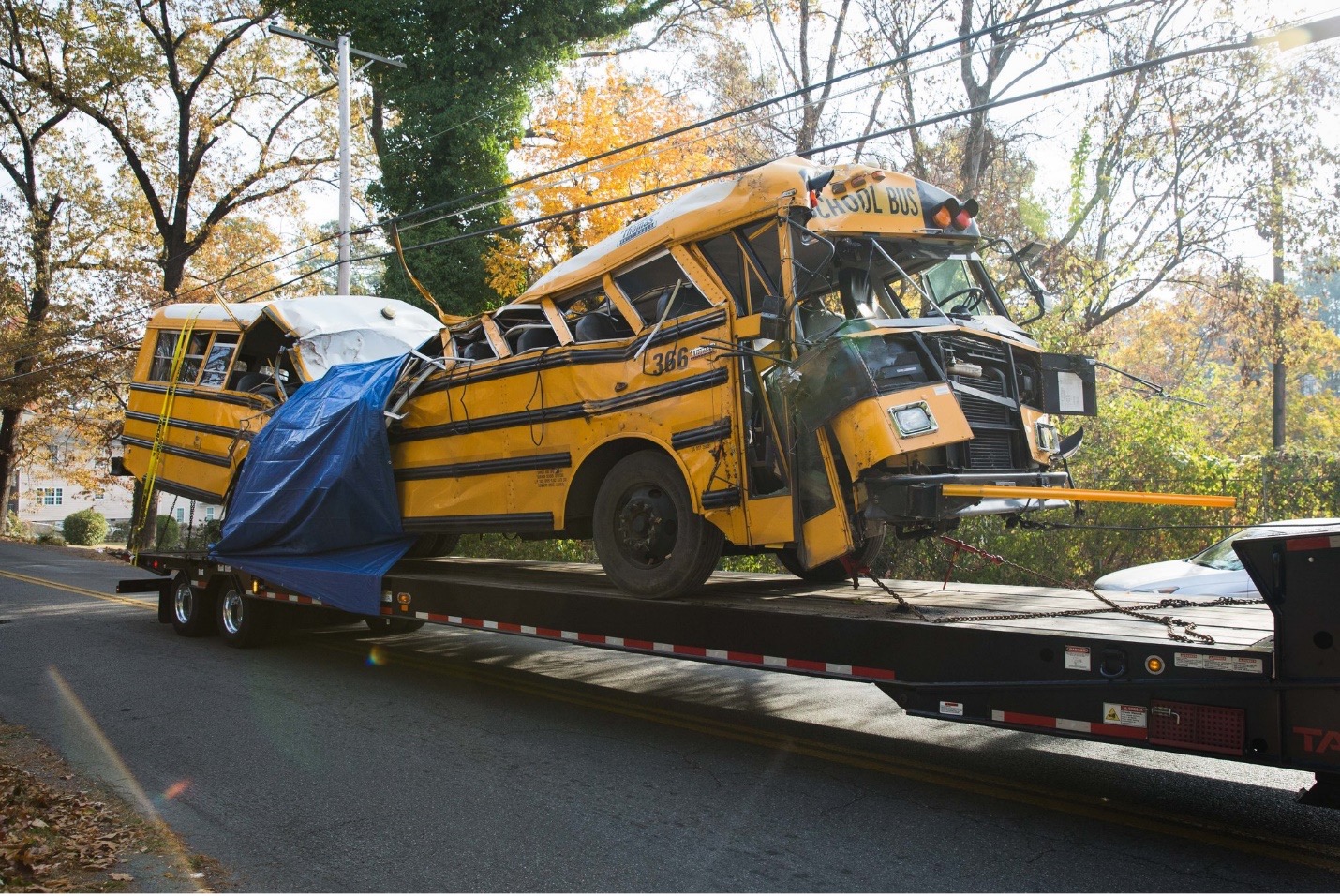 a severely damaged and crumpled school bus on the bed of a tow truck trailer
