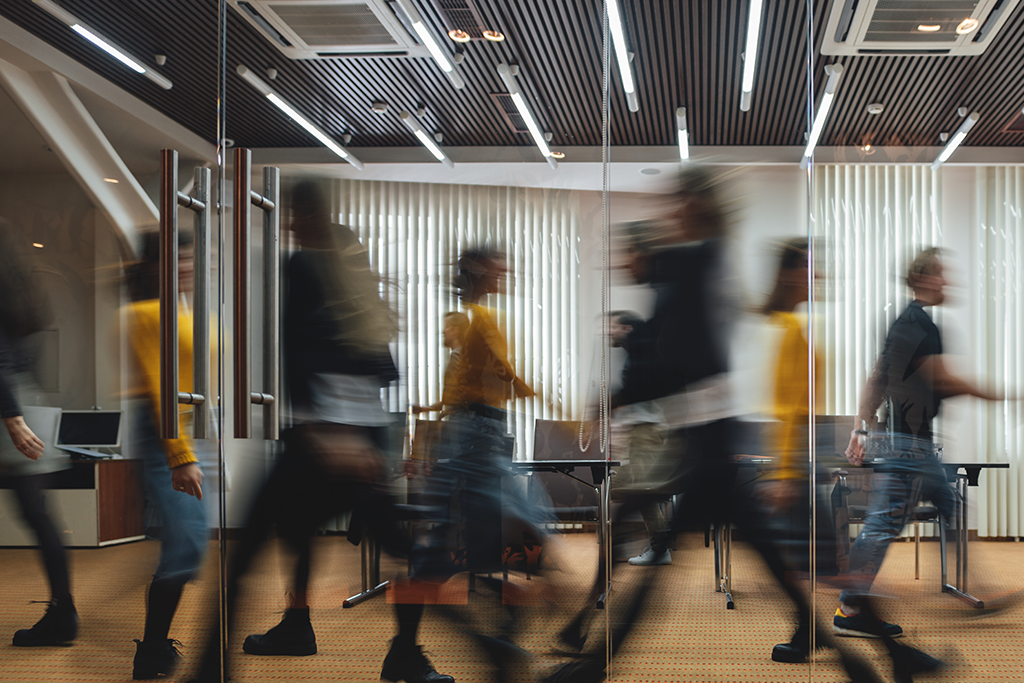 a busy office setting with people walking past conference rooms