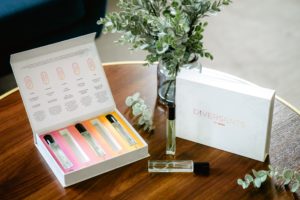 An open box of five colorful perfume bottles labeled ‘Diverscents’ on a table with a vase of greenery