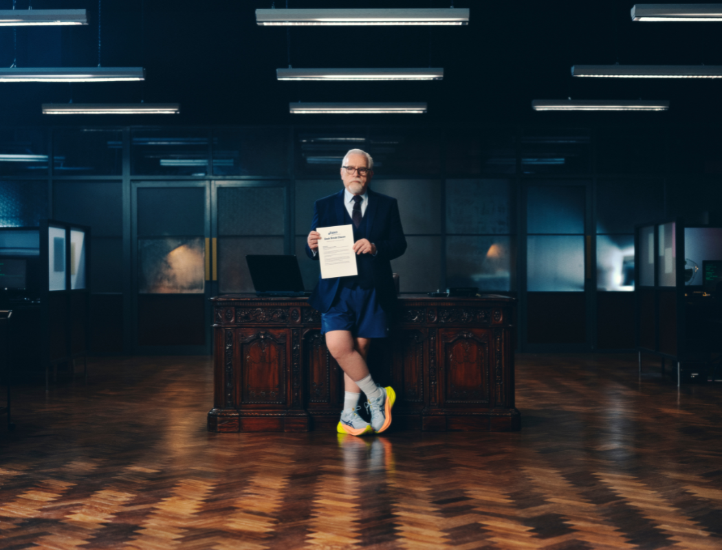 man in suit jacket with shorts and ASICS shoes on holding up a contract